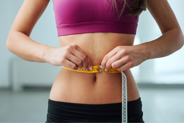 Slim young woman measuring her thin waist with a tape measure, close up